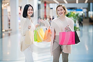 Two happy friends girls with shopping bags walking in mall