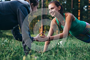 Two happy friends holding hands while doing plank exercise in park