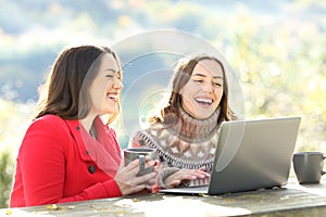 Two happy friends laughing watching laptop content in winter