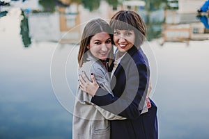Two happy friends or sisters hugging and looking at the camera on the street. Lifestyle outdoors. Port background