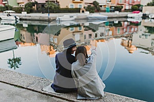 Two happy friends sitting on the dock at the port, having fun and talking on the street. Lifestyle outdoors