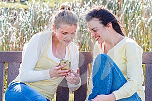 Two happy friends sitting on park bench talking and interacting.