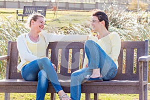 Two happy friends sitting on park bench talking and interacting.