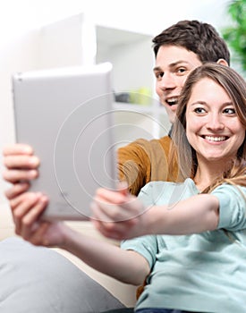 Two happy friends taking photo with tablet pc at home on the couch