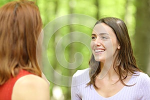 Two happy friends talking in a green forest or park