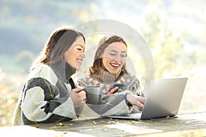 Two happy friends using laptop in winter in a park