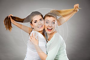 Two happy friends women hugging holding hair