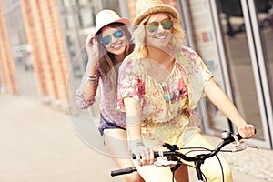 Two happy girl friends riding tandem bicycle