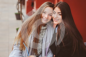 Two happy girl friends talking and drinking coffee in autumn city in cafe. Meeting of good friends, young fashionable students