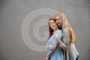 Two happy girlfriends are hugging on the background of a gray wall. Gentle hugs of a female lesbian couple. LGBT Same