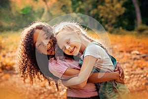 Two happy girls as friends hug each other in cheerful way. Little girlfriends in park.