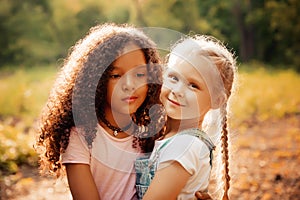 Two happy girls as friends hug each other in cheerful way. Little girlfriends in park.