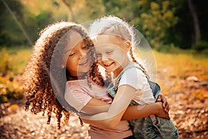 Two happy girls as friends hug each other in cheerful way. Little girlfriends in park.