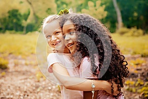 Two happy girls as friends hug each other in cheerful way. Little girlfriends in park.