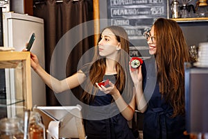 Two happy girls baristas holding donuts in their hands and making selfies