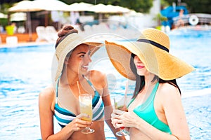 Two happy girls with beverages on summer party near the pool