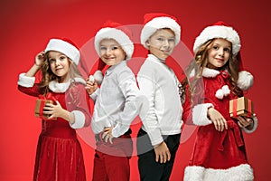 Two happy girls and boys in santa claus hats with gift boxes