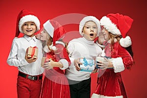 Two happy girls and boys in santa claus hats with gift boxes at studio