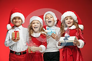 Two happy girls and boys in santa claus hats with gift boxes at studio