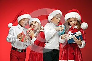 Two happy girls and boys in santa claus hats with gift boxes at studio