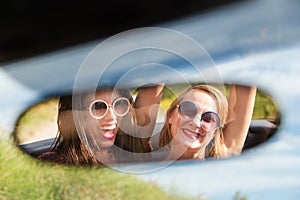 Two happy girls in a car rear-view mirror.