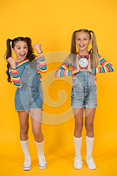 Two happy girls hold alarm clock. back to school. summertime. discipline and time management. teenage girls yellow wall