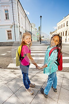 Two happy girls hold hands, stand near crossroad