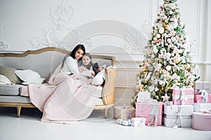 Two happy girls, mother and daughter siting on a sofa in Christmas decorated room.