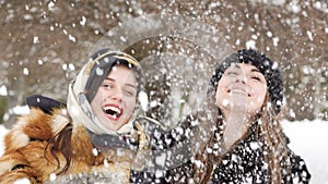 Two happy girls smiling and throwing up snow in the park. Slowly