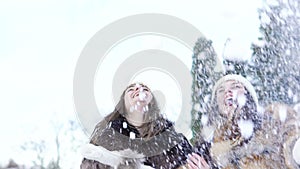 Two happy girls smiling and throwing up snow in the park. Slowly