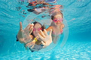 Two happy girls swimming under clear water of pool