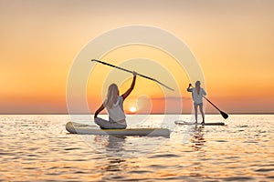 Two happy girls walks at sunset lake on sup boards