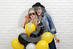 Two happy hipster girls in sunglasses have fun with balloons