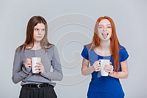 Two happy joking and sad frowning young women drinking tea