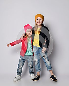 Two happy joyful smiling kids girls in bright stylish casual clothing, hats and sneakers pose together hugging