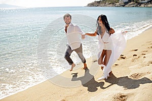 Two happy just married young adults, men holding his wife, running in the water, isolated on a seascape background.