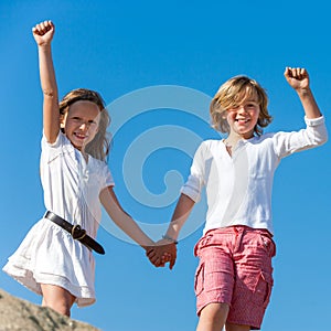 Two happy kids raising hands outdoors.