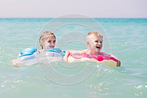 Two happy kids swim on the inflatable circles in the sea