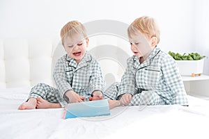 Two happy little boys brothers twins in pajamas reading book in their parents bed