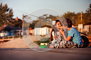 Two happy little friends, boy and girl eating sandwiches and fishing on a lake in a sunny summer day