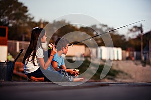 Two happy little friends, boy and girl fishing on a lake in a sunny summer day