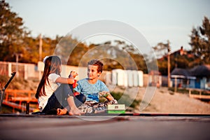 Two happy little friends, boy and girl talking, drinking tea, eating sandwiches and fishing on a lake in a sunny summer day