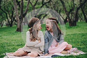 Two happy little girlfriends picking flowers in spring garden. Sisters spending time together outdoor.