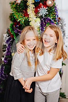 two happy little girls blonde at the Christmas tree. happy childhood