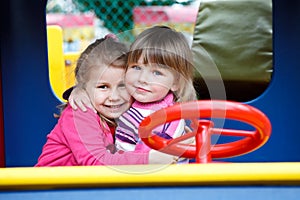 Two happy little girls embracing on playgroung