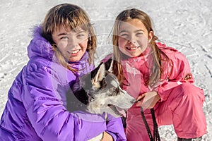 Two Happy little girls holding puppy dog husky on the snow