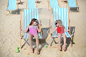 Two happy little girls lie on sun loungers and
