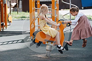 Two happy little girls playing with a spring horse on a children playground