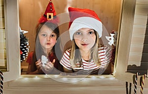Two happy little girls, sisters are playing in children`s playhouse with windows. Preparing for Christmas and New Year. Garlands,