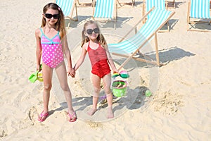 Two happy little girls stand on beach with toys at